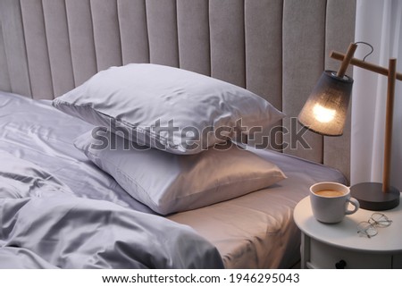 Cozy bed with soft silky bedclothes in light room Royalty-Free Stock Photo #1946295043
