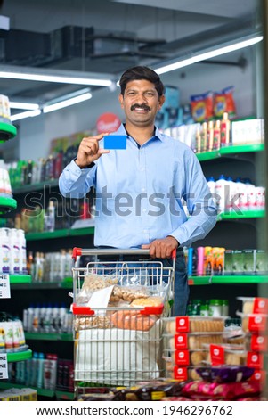 Happy grocery store owner holding credit card at store.