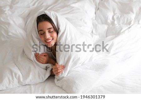 Cheerful young woman covered with warm white blanket lying in bed. Space for text Royalty-Free Stock Photo #1946301379