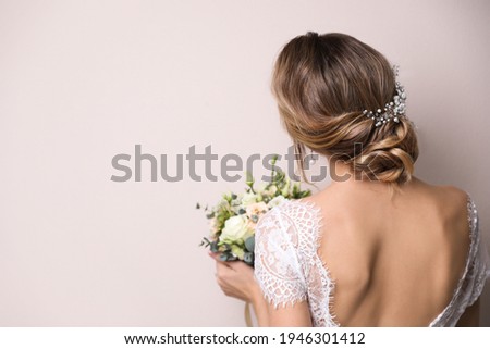 Young bride with elegant hairstyle holding wedding bouquet on beige background, back view. Space for text Royalty-Free Stock Photo #1946301412