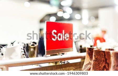 Red bright SALE sign in a womenswear store, surrounded by shoes and accessories. Seasonal discount offer at retail shopping mall. Soft focus, close up, copy space