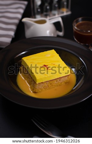 Saffron cake with saffron in the top
and saffron sauce in black plate and cup of saffron sauce and napkin on black background 