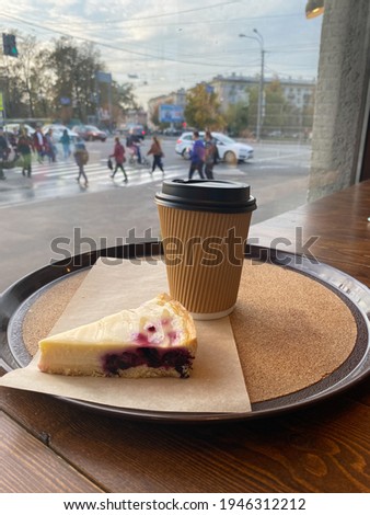 A glass of coffee and a berry cheesecake by the window overlooking the pedestrian crossing.
