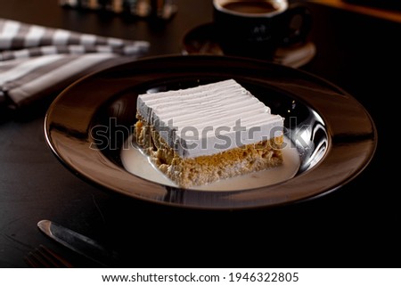 vanilla milk cake with strawberry in the top and sauce in black plate and cup of coffee
