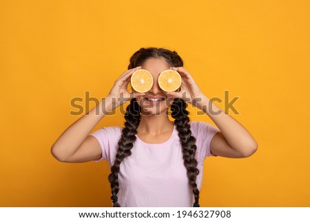 Healthy Nutrition Concept. Funny smiling young indian woman holding halves of citrus juicy fruits and covering eyes, making glasses from orange, isolated over bright yellow studio background Royalty-Free Stock Photo #1946327908
