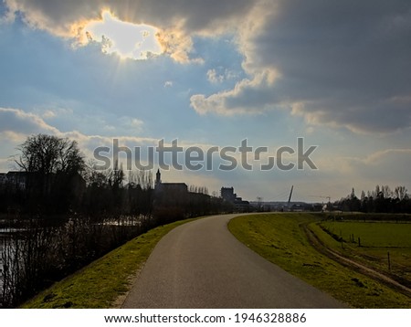 Towpath along river Scheldt with silhouette of church and skyscrapers under low evening sun in Wetteren