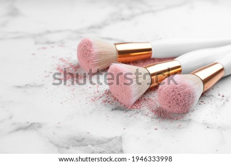 Different makeup brushes with crushed cosmetic product on white marble table, closeup. Space for text