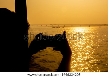 A traveler is taking pictures of the newly built Padma multipurpose bridge using his smartphone in the against sunlight.