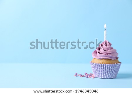 Delicious birthday cupcake with burning candle and sprinkles on light blue background, space for text