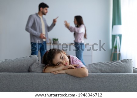 Family conflicts. Sad arab girl sitting alone, feeling lonely and depressed while her parents arguing on the background, selective focus. Family crisis and relationship problems Royalty-Free Stock Photo #1946346712
