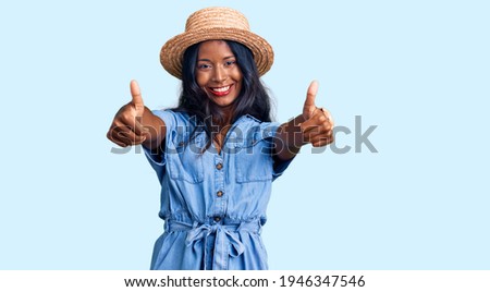 Young indian girl wearing summer hat approving doing positive gesture with hand, thumbs up smiling and happy for success. winner gesture. 