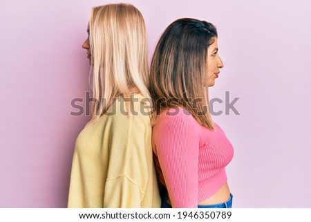 Two friends standing together over pink background looking to side, relax profile pose with natural face with confident smile. 