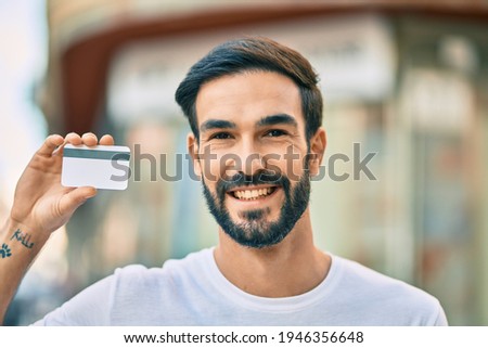Young hispanic man smiling happy holding credit card at the city.