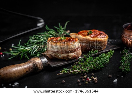 Medallions steaks from the beef tenderloin covered bacon on old meat butcher on Dark background. Top view.