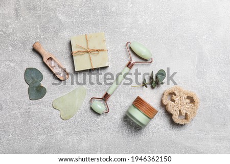 Flat lay composition with face roller and cosmetic products on light grey stone table