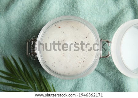 Jar of salt scrub and palm leaf on green towel, flat lay