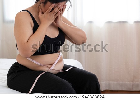 Overweight Women stressing over fat belly, using measuring tape. Overweight Woman Measuring Waist. Fat woman with tape measure, she uses her hand to squeeze the excess fat, surprise obese female.  Royalty-Free Stock Photo #1946363824