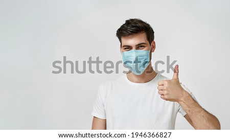 Everything okay. Young man wearing medical mask showing the thumbs up, super sign on a grey isolated background. Coronavirus prevention concept
