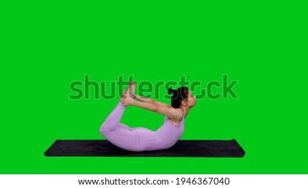 Young sporty fit woman in bodysuit doing yoga bow pose on mat against green screen background