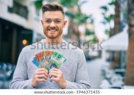 Young caucasian man smiling happy holding australian dollars at the city.