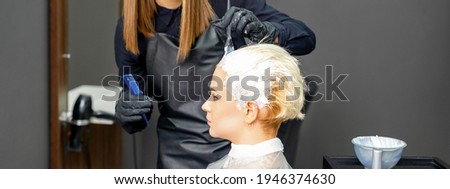 Female hairdressers dyeing hair of young caucasian woman in hair salon