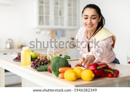 Healthy Food To Boost Your Immune System. Beautiful smiling young woman cooking fresh organic salad at home in modern kitchen, reaching for vegetables, copy space. Diet, Food And Lifestyle Concept Royalty-Free Stock Photo #1946382349