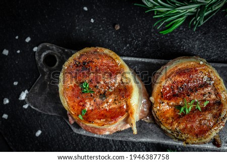 Medallions steaks from the beef tenderloin covered bacon on old meat butcher on Dark background. Top view.