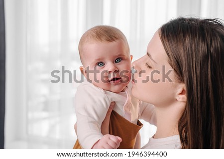 Close up of loving tender young mum holding adorable cute baby girl. Portrait happy affectionate caucasian mother cuddling with infant child daughter standing near window at home
