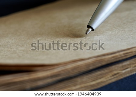Ballpoint pen tip next to eco-friendly recycled notebook. Concept for creativity, memory, study, spelling, writing a letter, book or script. Macro. Selective focus Royalty-Free Stock Photo #1946404939