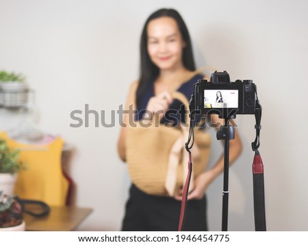 Asian woman  working at home,  using camera  to live or record video selling her woven bag. Indoor,  selective focus. Business and online selling concept.