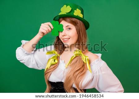 Portrait of woman in festive costume and St. Patrick's day hat holding shamrock isolated on green background.