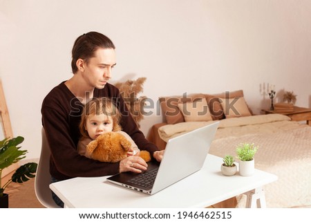 A man works at home on a laptop. The child distracts from work, misses. The father and his daughter are sitting at the computer. Two-year-old girl hugs soft toy sad Freelance beige interior