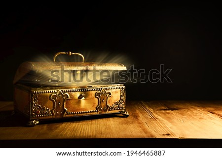 Image of mysterious magical treasure chest with light over wooden old table and dark background