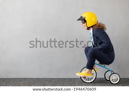 Successfull businesswoman driving toy car outdoor. Funny young woman against concrete wall background. Business srart up and winner concept Royalty-Free Stock Photo #1946470609
