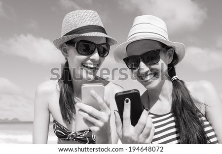 Girls using smart phone at the beach. Holiday and technology concept.