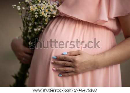 a woman in a pink dress and daisy flowers in her hand. Waiting for a baby, pregnant photo session. pregnancy and childbirth in the summer, 9 months. Gender party, pink and blue nails. selective focus