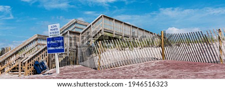 Wooden staircase for walkway over the sand dunes on a Fire Islands Beach with signs reading alcohol prohibited and no lifeguard on duty.