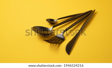 Black kitchen cutlery set. Stylish tableware on yellow cloth. Yellow background with black matte cutlery