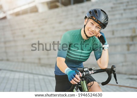 Happy professional female cyclist in protective gear smiling at camera while standing with her bike outdoors on a daytime Royalty-Free Stock Photo #1946524630