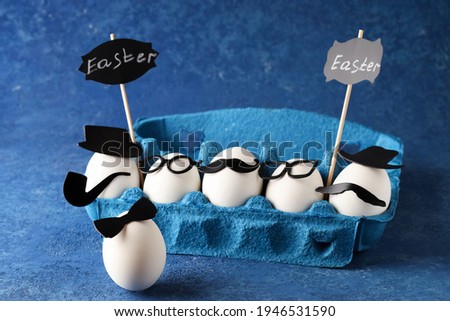 White eggs of a chicken farm in a cardboard blue market box on a solid background. Cheerful company of figures in the concept of the creative holiday of Easter