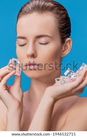 Closeup portrait of beautiful young woman applies the ice to face on a blue background. High quality photo