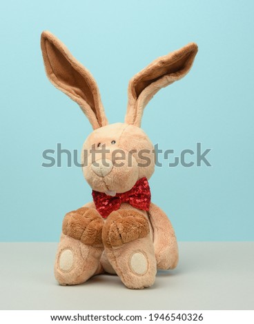 cute plush hare with long ears, a red butterfly tied around the neck, blue background