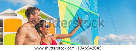 Happy summer couple taking selfie on Florida beach on travel vacation. Sunbathing woman in bikini using phone with man friend. Panoramic banner.