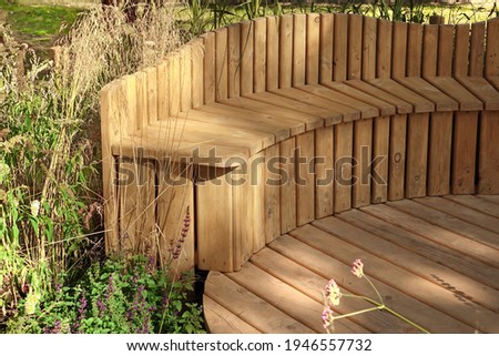 Backyard Wooden Patio with Rounded Bench. Designed Garden Surface. Landscaped Garden with Wooden Elements. Designed Patio or Terrace. Hardwood Decking or Flooring.