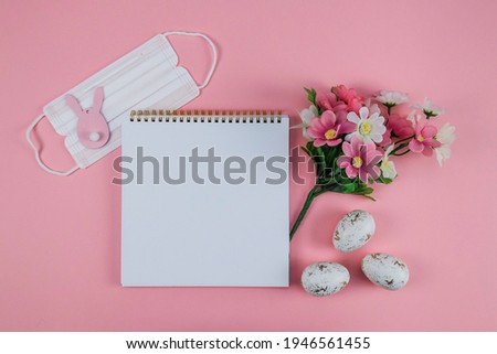 Empty notebook with spring flowers, medical mask and Easter bunny lie on a pink background with place for text, top view close-up.