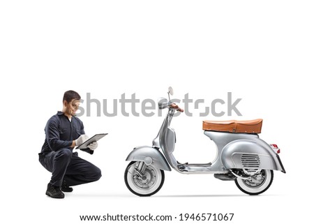 Motorbike mechanic kneeling and checking a vintage model scooter isolated on white background Royalty-Free Stock Photo #1946571067
