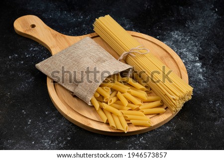 Penne pasta in a rustic basket with spaghetties on a wooden platter