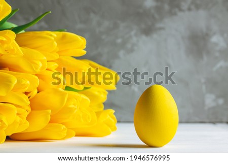 Bouquet of bright yellow tulips and Easter egg, standing on white wooden surface on gray background, copy space