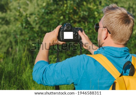A mock-up of a reflex camera in the hands of a Guy in the forest. Against the backdrop of beautiful greenery