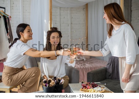 Three happy female friends drinking champagne cheers together laughing having positive emotion low angle. Smiling woman holding glass with cold alcohol beverage rejoicing gossiping enjoying friendship